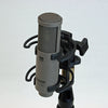 This is a photo of the Sanken CU-55 microphone. It is shown in a grey colour. It is held in place by a piece of black equipment at an angled front view.